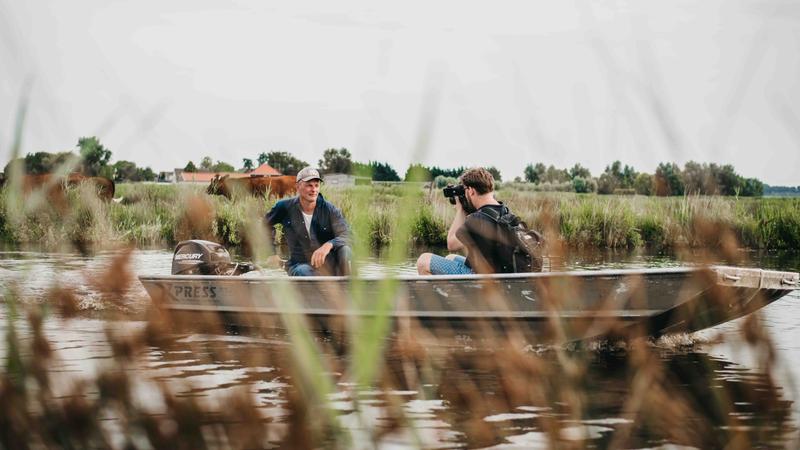 Twee mensen in een boot, gefilmd op het water, natuur op de voorgrond Persoon wordt gefilmd in een boot