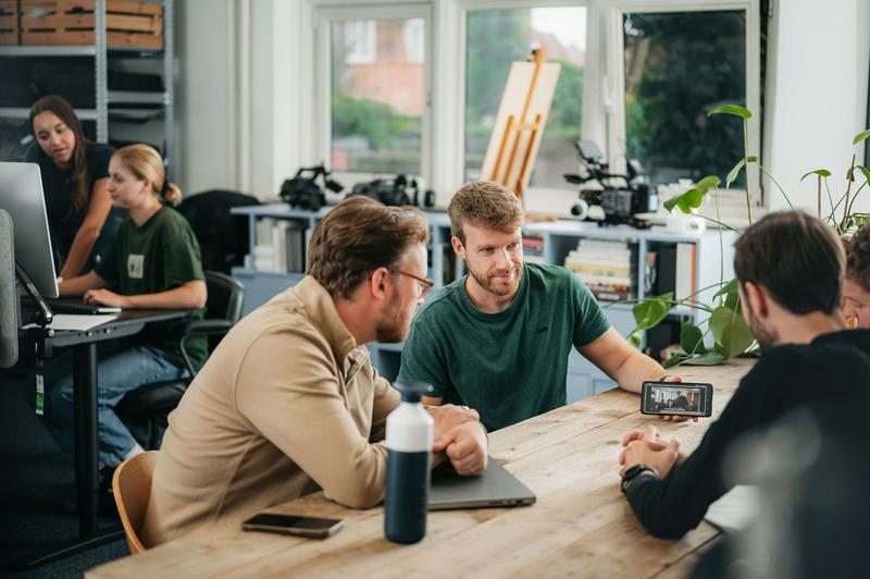 Drie mannen bekijken samen een video op een smartphone aan een houten tafel in een kantoor Video crew bekijkt video