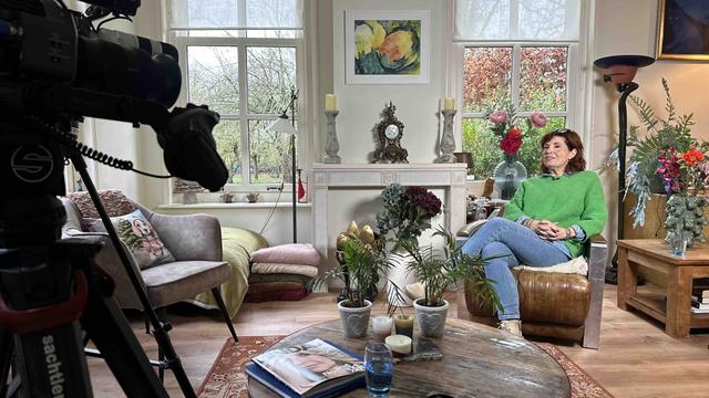 Interviewopname in huiselijke setting Vrouw zit in een woonkamer en wordt gefilmd tijdens een interviewopname, met een videocamera op de voorgrond