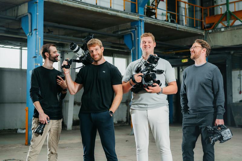 Vier mannen met camera’s staan samen in een industriële hal Vier videografen staan met camera-apparatuur in een industriële omgeving