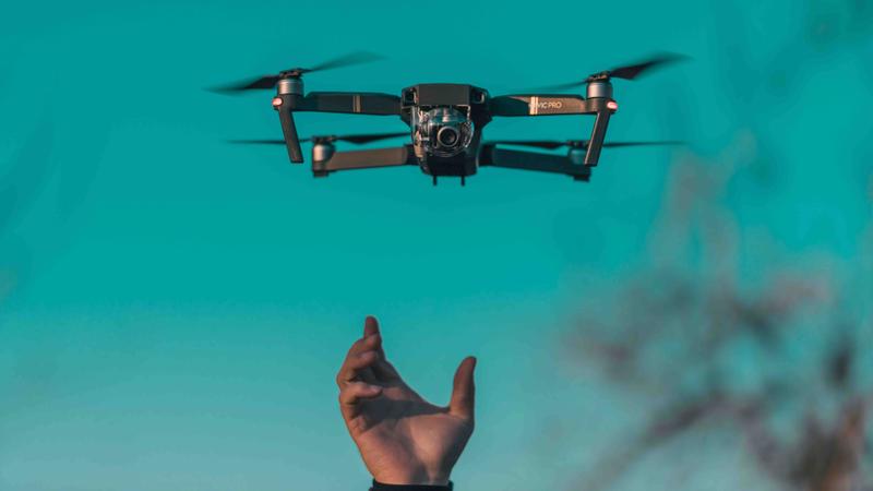 Drone in de lucht met hand eronder Drone vliegt in de lucht terwijl een hand zichtbaar is onder het toestel